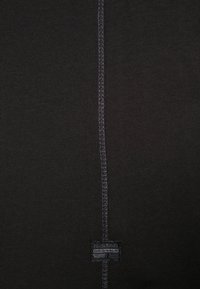 Black t-shirt with a straight seam down the center, featuring a textured patch with the brand name in white, and a soft, cotton-like material.