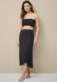 Zwart tweedelig outfit met een strapless, gesmokte bandeau top en een midi rok met een zijslit, gemaakt van een zachte, lichte stof.