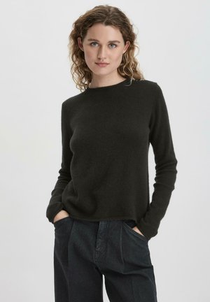 Schwarzer Strickpullover mit langen Ärmeln und Boot-Ausschnitt. Der Stoff sieht weich aus, mit einer glatten Textur, kombiniert mit hoch taillierten dunklen Jeans.