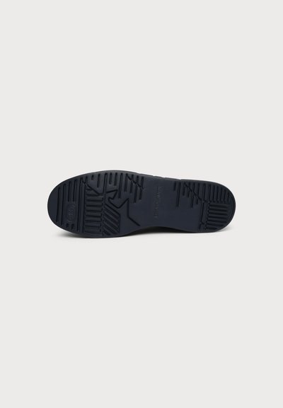 Semelle de chaussure en caoutchouc noir avec motif de bande de roulement comprenant des rainures géométriques et de petites zones texturées sur fond blanc.