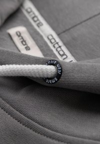 Šedá bavlněná mikina s kapucí má texturovanou tkaninu, bílou šňůrku a černou očko s brandingem "ombre wear". Vnitřní štítek zobrazuje "ombre cotton."