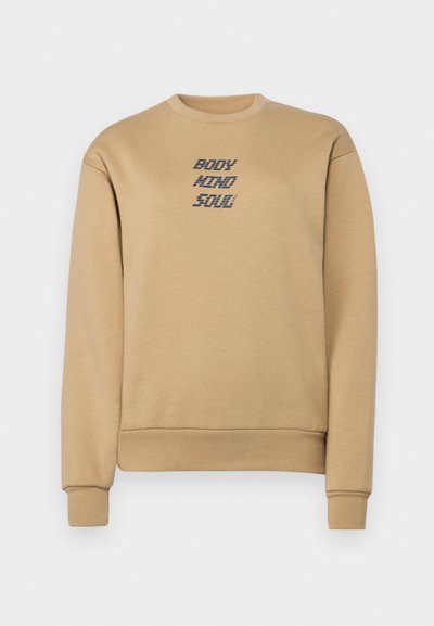 Sudadera beige con cuello redondo, puños y dobladillo acanalados. Texto "Cuerpo Mente Alma" impreso en azul oscuro en el pecho. Textura suave.