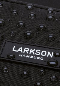 Tissu noir texturé avec des gouttes d'eau. Présente une étiquette rectangulaire avec "LARKSON" en blanc sur fond noir.