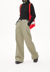 Pantalon large kaki en coton, associé à un pull noir côtelé. Un sac fourre-tout matelassé rouge vif complète la tenue.