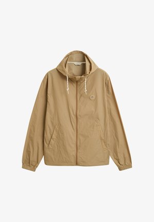 Chaqueta ligera color marrón claro con capucha, cierre de cremallera, puños elásticos y bolsillos laterales. Presenta un pequeño logo redondo en la zona del pecho izquierdo.