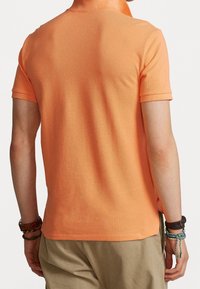Short-sleeve polo shirt in vibrant orange, featuring a textured knit, ribbed collar, and straight hem. Worn with light-colored shorts.