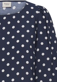 Tissu bleu marine à pois blancs, encolure arrondie et épaules légèrement froncées.