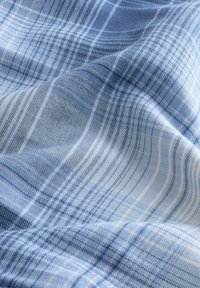 Tissu en plaid bleu clair avec des nuances variables de bleu et des lignes blanches. Texture douce avec un tombé fluide, présentant un motif tissé.