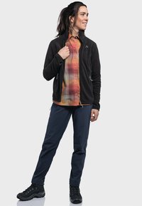 Schwarze Fleecejacke, kariertes Hemd in Orange und Gelb, marineblaue Hose und schwarze Wanderstiefel. Verfügt über Reißverschlüsse und eine enge Passform.