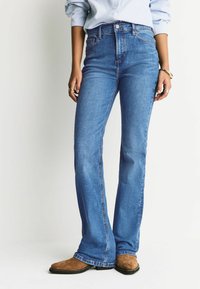 Blugi evazați cu talie înaltă din denim albastru mediu, cu design clasic cu cinci buzunare, detalii cusute și închidere cu nasturi.