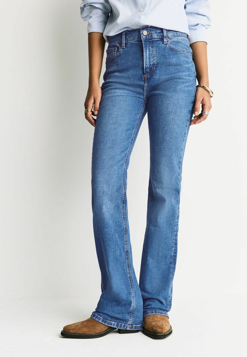 Blugi evazați cu talie înaltă din denim albastru mediu, cu design clasic cu cinci buzunare, detalii cusute și închidere cu nasturi.