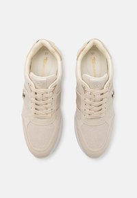 Beige sportieve schoenen gemaakt van textuurmateriaal, met veters, een glanzend gouden accent en een witte zool met subtiele stiksel details. Maat 37.