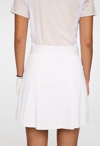 Gonna plissettata bianca con elastico in vita, realizzata in tessuto leggero, caratterizzata da una trama liscia e un design pulito e minimalista.