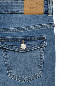Jeans de mezclilla en un color azul claro, con tela texturizada, un parche de cuero marrón con logo y costuras en contraste a lo largo de las costuras.