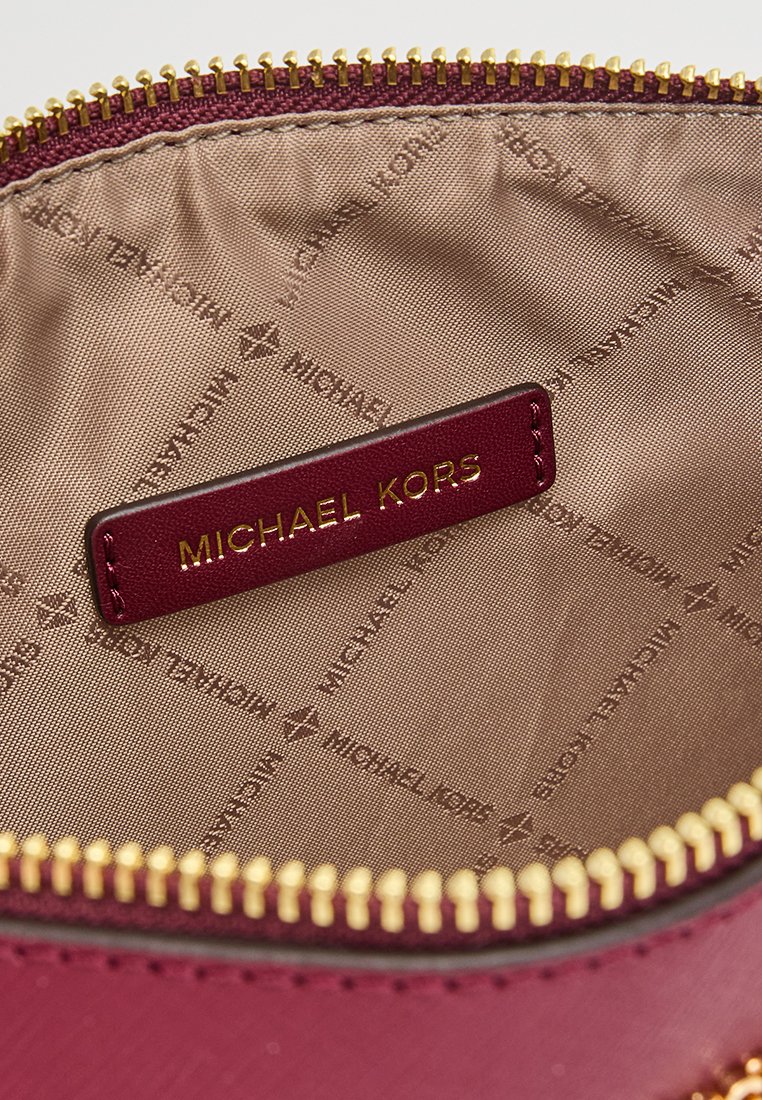 Interno di una borsa in pelle bordeaux con una cerniera dorata. Presenta una patch con logo dorato e una fodera in tessuto testurizzato con un motivo a ripetizione del nome del marchio.