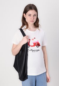 Bijela majica kratkih rukava s grafikom crvenog skutera ukrašenog šljokicama, u kombinaciji s svijetloplavim trapericama i crnom torbom preko ramena.