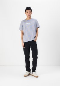 T-shirt à manches courtes rayé bleu et gris avec un logo blanc, assorti à un jean noir et des baskets blanches avec des semelles en gomme. Design simple et décontracté.