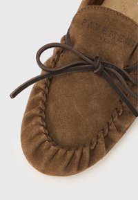 Mocassin en daim marron avec bordure cousue et lacets en cuir. Doté d'un bout arrondi et d'une texture douce. Nom de la marque embossé sur la languette.