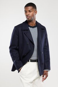 Granatowy dwurzędowy płaszcz wełniany z szerokimi klapami, dużymi guzikami i bocznymi kieszeniami, połączony z pasiastą koszulą i kremowymi spodniami.