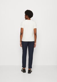 T-shirt bianco a maniche corte abbinato a pantaloni slim-fit blu navy, mostrato da dietro. Il tessuto appare liscio con una vestibilità rilassata. Scarpe nere.
