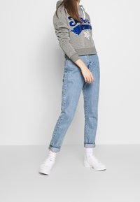 Gray hoodie with blue sequined text, drawstring hood, and ribbed cuffs. Paired with light blue high-waisted jeans and white sneakers.