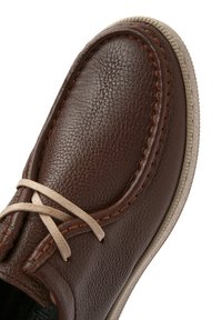 Scarpa in pelle marrone con finitura testurizzata, lacci beige e cuciture a contrasto, dotata di punta rotonda e suola di colore chiaro.
