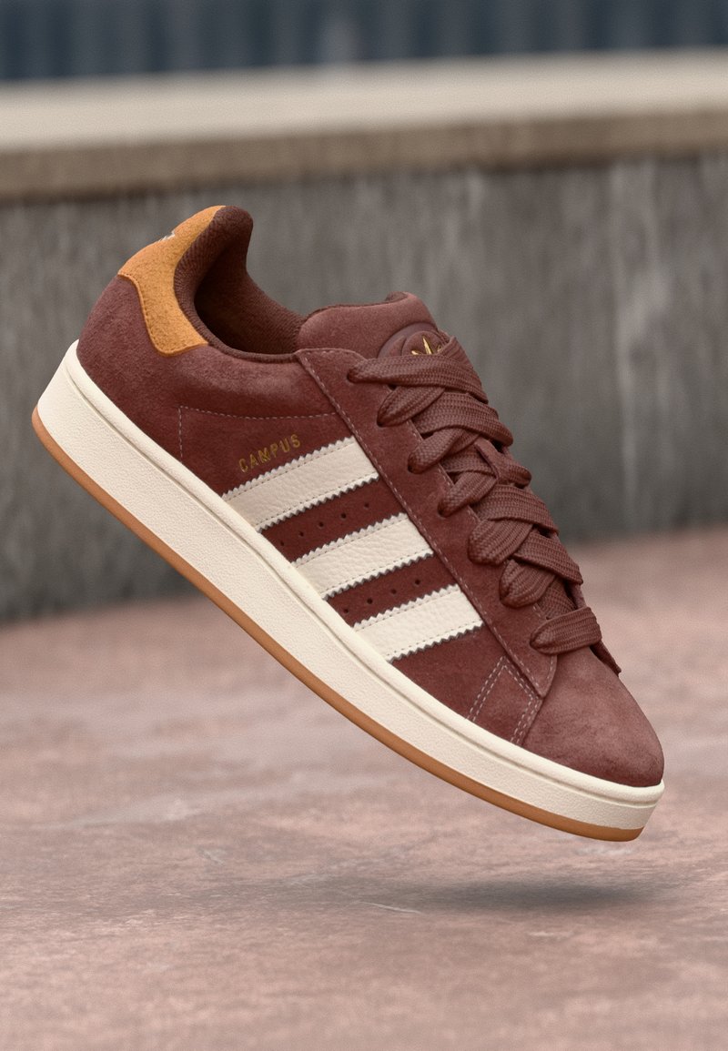 Brune ruskinds sneakers med hvidt tredobbelt stribedesign, beige sål, rund tå og polstret krave. Har guld "CAMPUS" branding på siden.