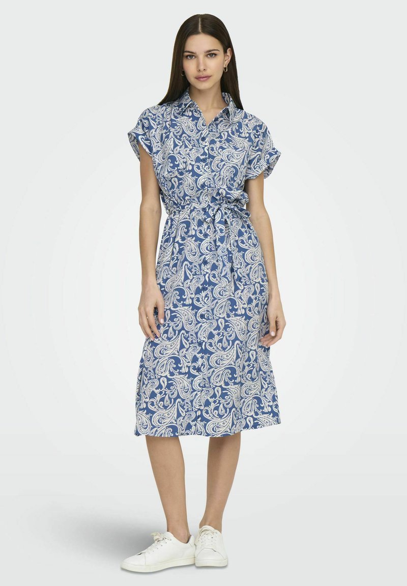 Abito blu con fantasia paisley, maniche corte, colletto e dettaglio in vita con fiocco, abbinato a sneakers bianche. Texture liscia.