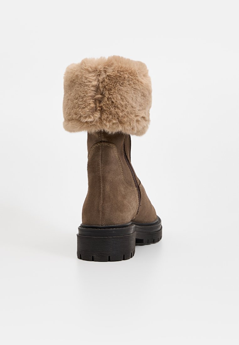 Bruine suede enkellaars met een fluffy beige nep bont kraag, heeft een zijrits en een stevige zwarte rubberen zool met textuurdetails.