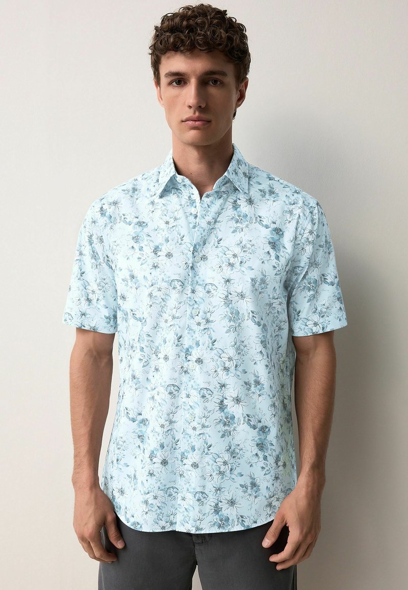 Camicia a maniche corte in tessuto azzurro chiaro con un motivo floreale in tonalità più scure, dotata di colletto button-down e orlo dritto.
