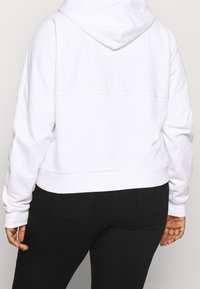Felpa bianca corta con una texture morbida, dotata di cappuccio con coulisse e polsini a coste, abbinata a pantaloni neri slim-fit.