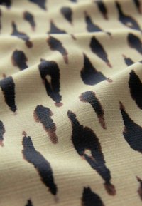 Lys beige stof med et sort og brunt dyreprint. Teksturen ser glat ud med en let glans og fald.