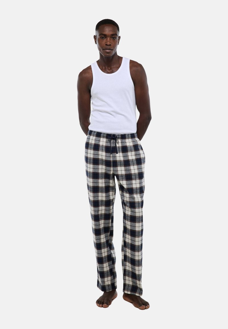 Débardeur blanc associé à un pantalon de pyjama à carreaux bleu et crème, avec taille élastique et cordon de serrage, coupe décontractée et texture douce.