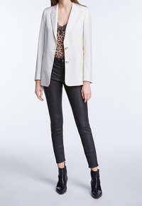 Blazer bianco sartoriale con due bottoni tono oro, abbinato a un top in pizzo con stampa leopardata, pantaloni skinny in pelle nera e stivaletti alla caviglia.