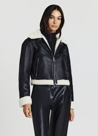 Veste en cuir noire courte avec un col et des poignets en peau de mouton, dotée d'une fermeture éclair et de poches latérales. La texture est lisse et brillante.