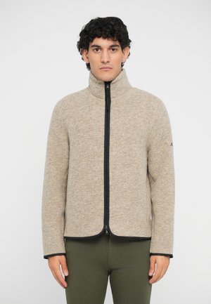 Beige fleecejakke med høy krage, svart glidelås og kontrastfargede svarte detaljer. Har lange ermer og en jevn, myk tekstur.
