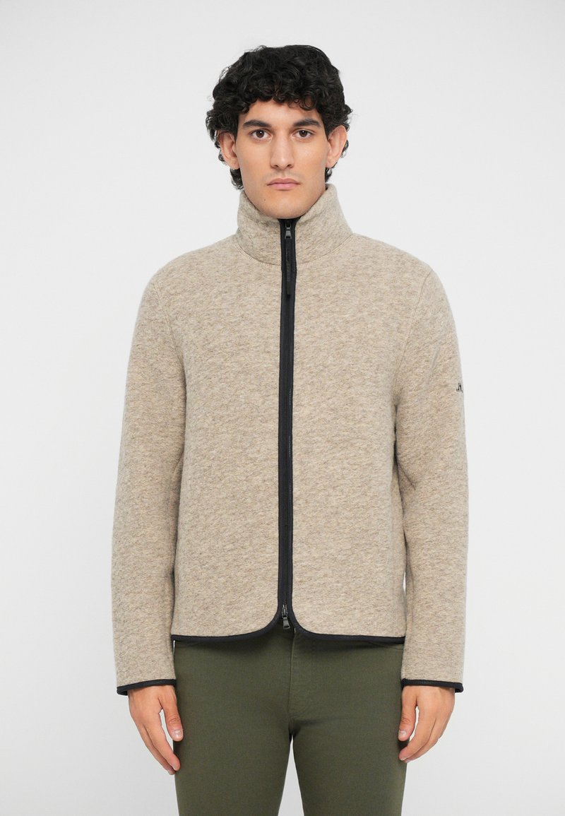 Beige fleece jacket with a high collar, black zipper, and contrasting black trim. Features long sleeves and a smooth, soft texture.