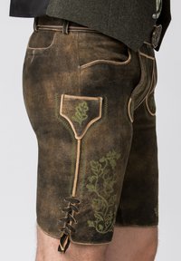 Bruine leren lederhosen met groene bloemenborduursels, een zak met bies en vetersluiting aan de zoom. Getextureerd, traditioneel ontwerp.