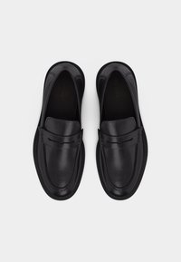 Mocassins en cuir noir avec bouts arrondis et couture moc toe, vus de dessus sur un fond blanc.