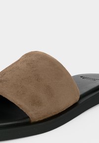 Sandale à enfiler avec une large bride en suède marron sur une semelle noire matelassée, conçue pour un usage décontracté.