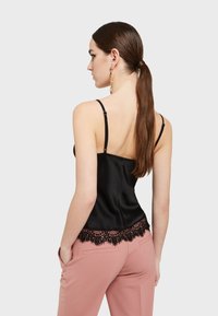 Černá saténová tílko s tenkými ramínky, ozdobené černou krajkovou lemovkou. Nosené s světle růžovými kalhotami s přesně padnoucím střihem, které mají jemnou strukturu.