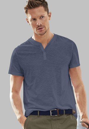 Marineblaue Kurzarm-Henley-Shirt mit einem Dreiknopfverschluss. Glatte Textur, lässige Passform, kombiniert mit einem gewebten Gürtel und grünen Hosen.