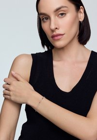 Srebrna bransoletka z delikatnym łańcuchem, z małymi akcentami i zapięciem, noszona na nagim nadgarstku w zestawieniu z czarnym swetem.