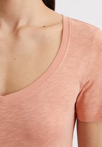 T-shirt a collo V in pesca realizzato in morbido tessuto testurizzato, con maniche corte e una silhouette aderente, caratterizzato da un collo pulito e una leggera elasticità.