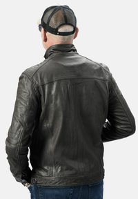 Zwarte leren jas met hoge kraag, gewatteerde schouderaccenten en een fitted design. Zichtbare hardware en stiksels benadrukken de textuur.