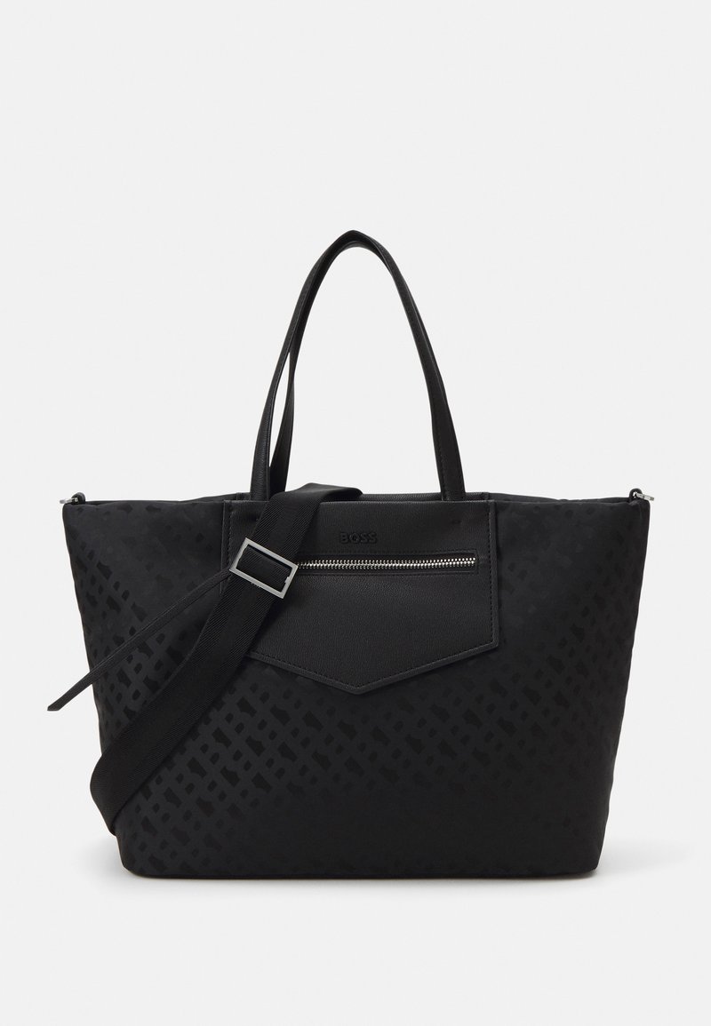 Sac fourre-tout noir en matériau texturé, doté d'une poche avant zippée, de doubles poignées et d'une bandoulière amovible. Design épuré.