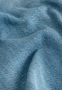 Gros plan sur un tissu en denim bleu clair montrant la texture et le tissage avec des plis doux et des variations subtiles de couleur.