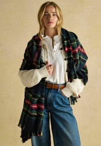 Ruuduline sall rohelises, punases ja kollases toonis, kantud valge särgi ja tekstuurse kreemikaardiiganiga. Sinised teksad ja pruun nahast vöö täiendavad välimust.