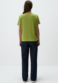 T-shirt verde a maniche corte realizzato in tessuto morbido, abbinato a jeans a gamba larga di colore blu scuro con tasche posteriori. Senza motivi visibili.