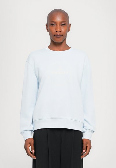 Sweatshirt bleu clair avec un col rond et des manches longues, présentant un imprimé graphique en or pâle. Le matériau semble doux et texturé.